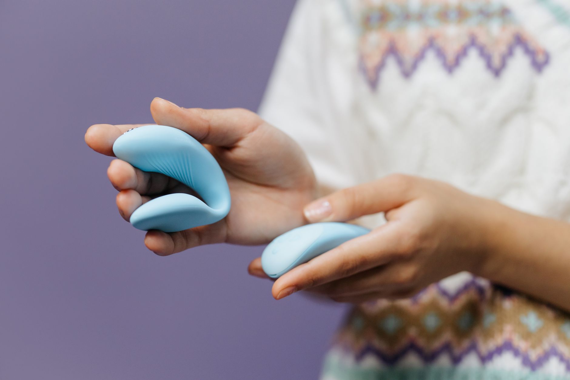 Manos sosteniendo un vibrador de succión azul contra un fondo púrpura, mostrando intimidad y placer