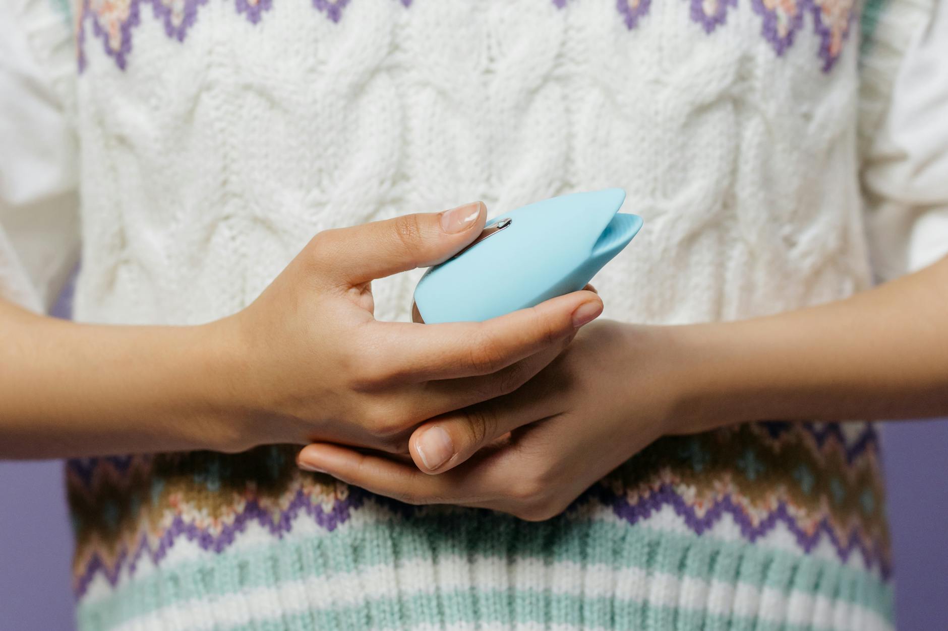 Persona sosteniendo un vibrador azul contra un suéter tejido