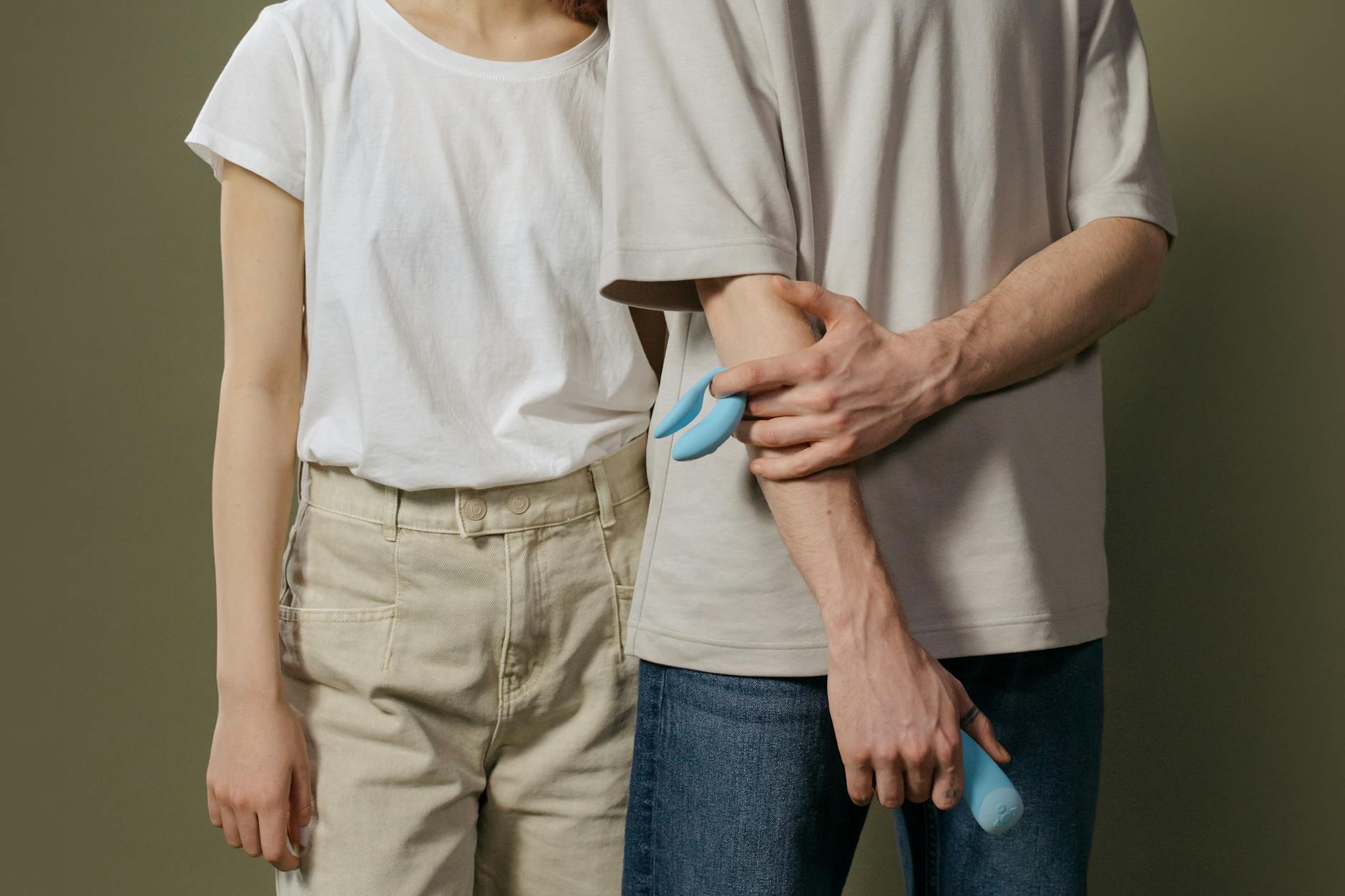 Una joven pareja de pie juntos en interiores, sosteniendo un vibrador azul, simbolizando la intimidad moderna.