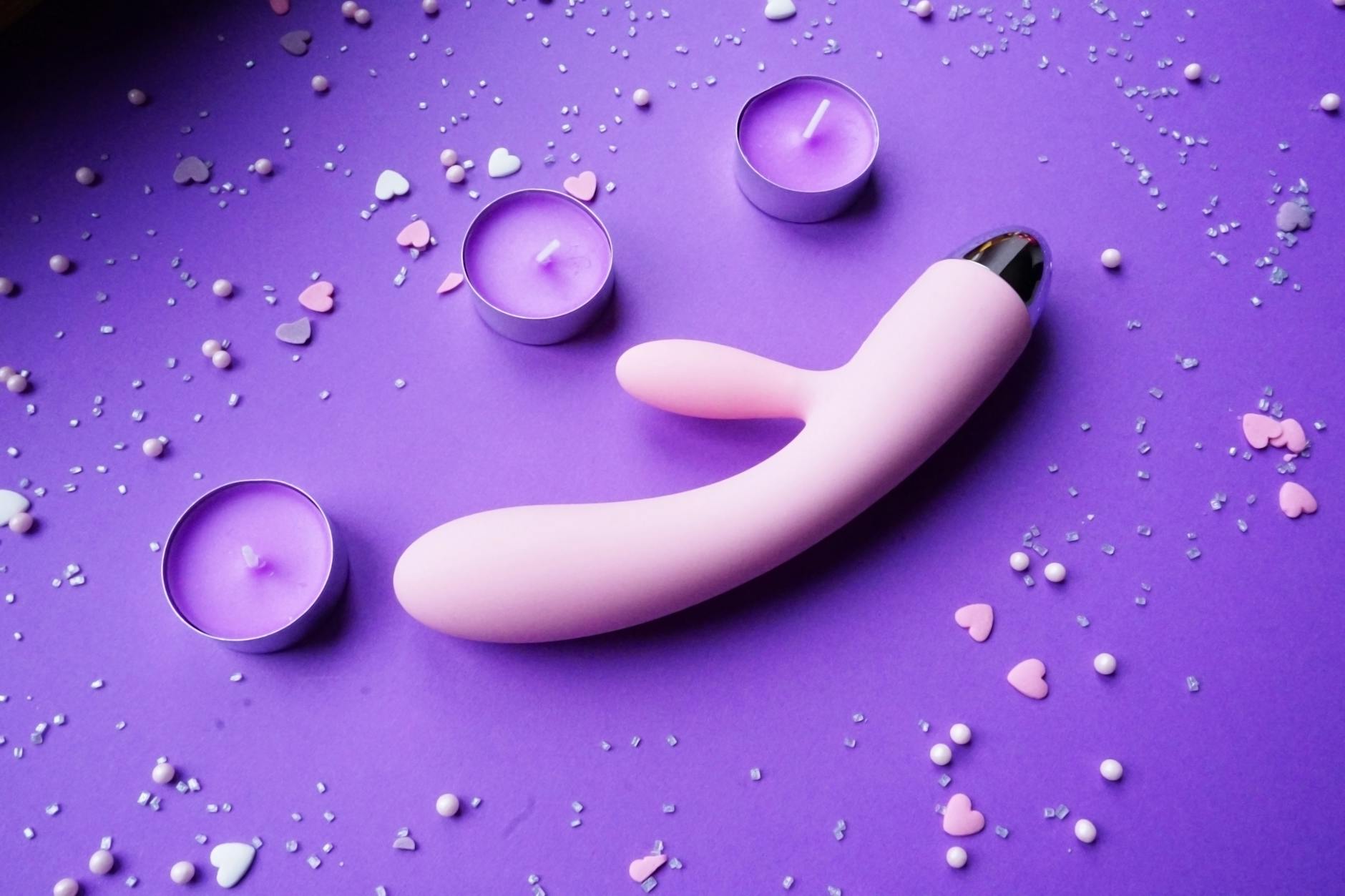 Vibrador rosa en fondo púrpura con confeti de corazones y velas para un ambiente romántico